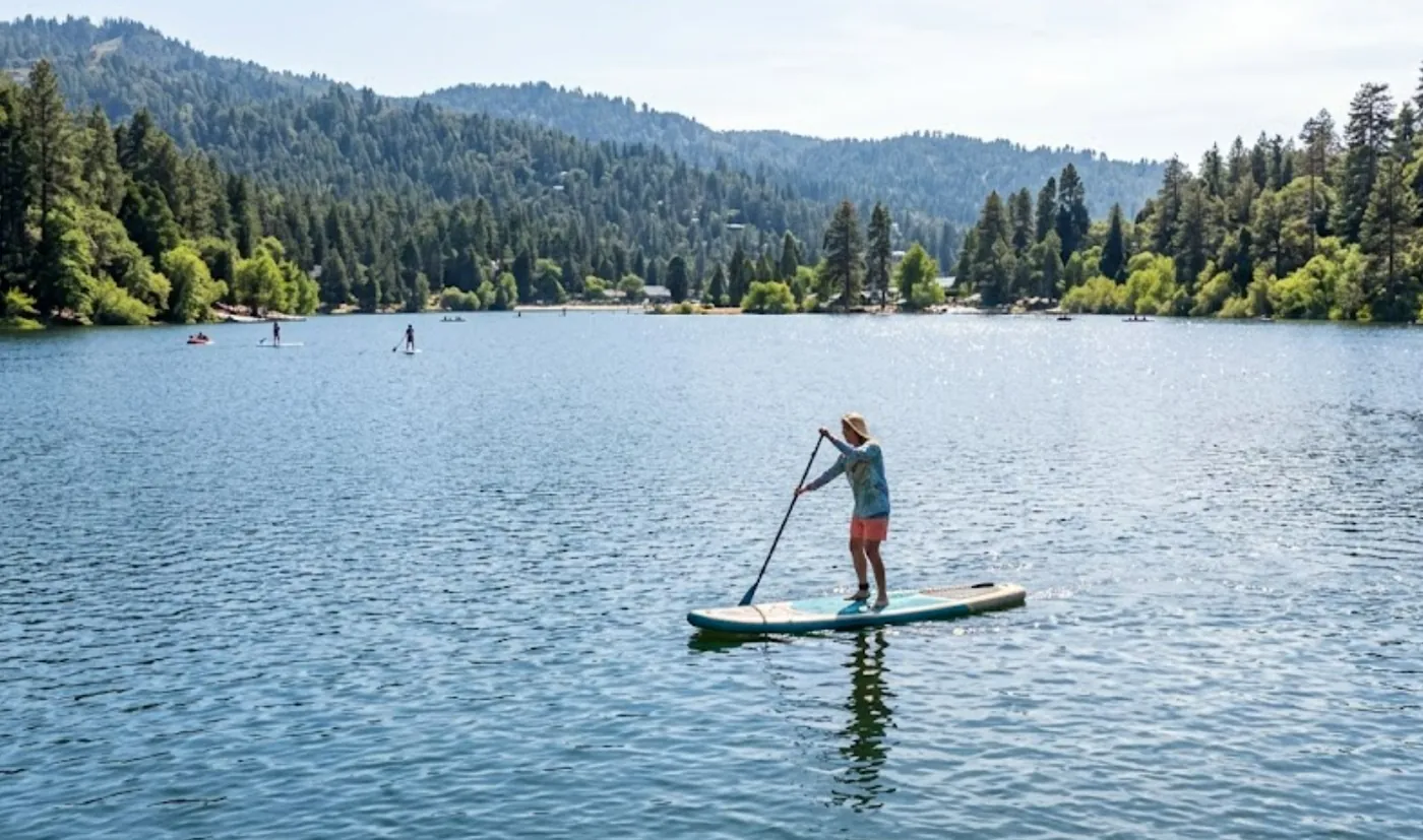 A stand-up paddleboarder crossing Lake Gregory below the pine ridgeline